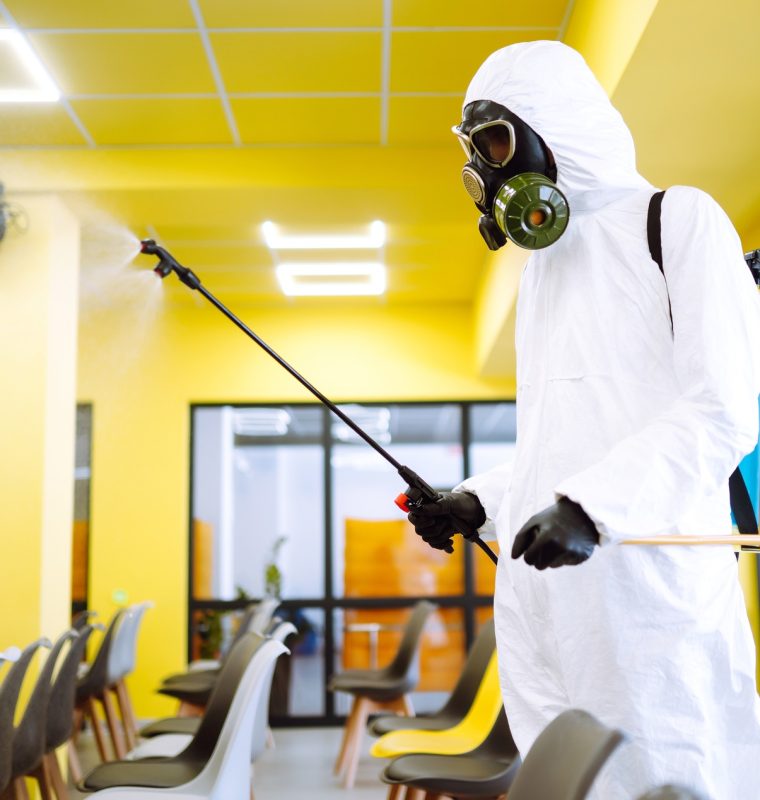 Man wearing protective suit disinfecting assembly hall with spray. Disinfecting of office. COVID-19.