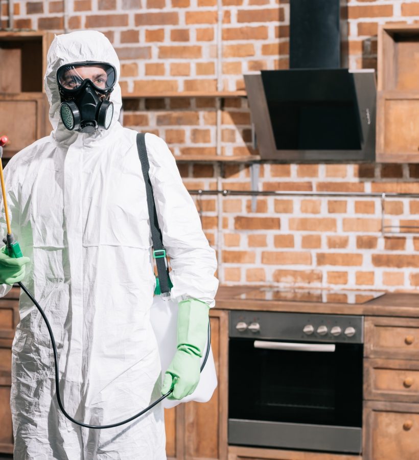 pest control worker standing with sprayer in kitchen